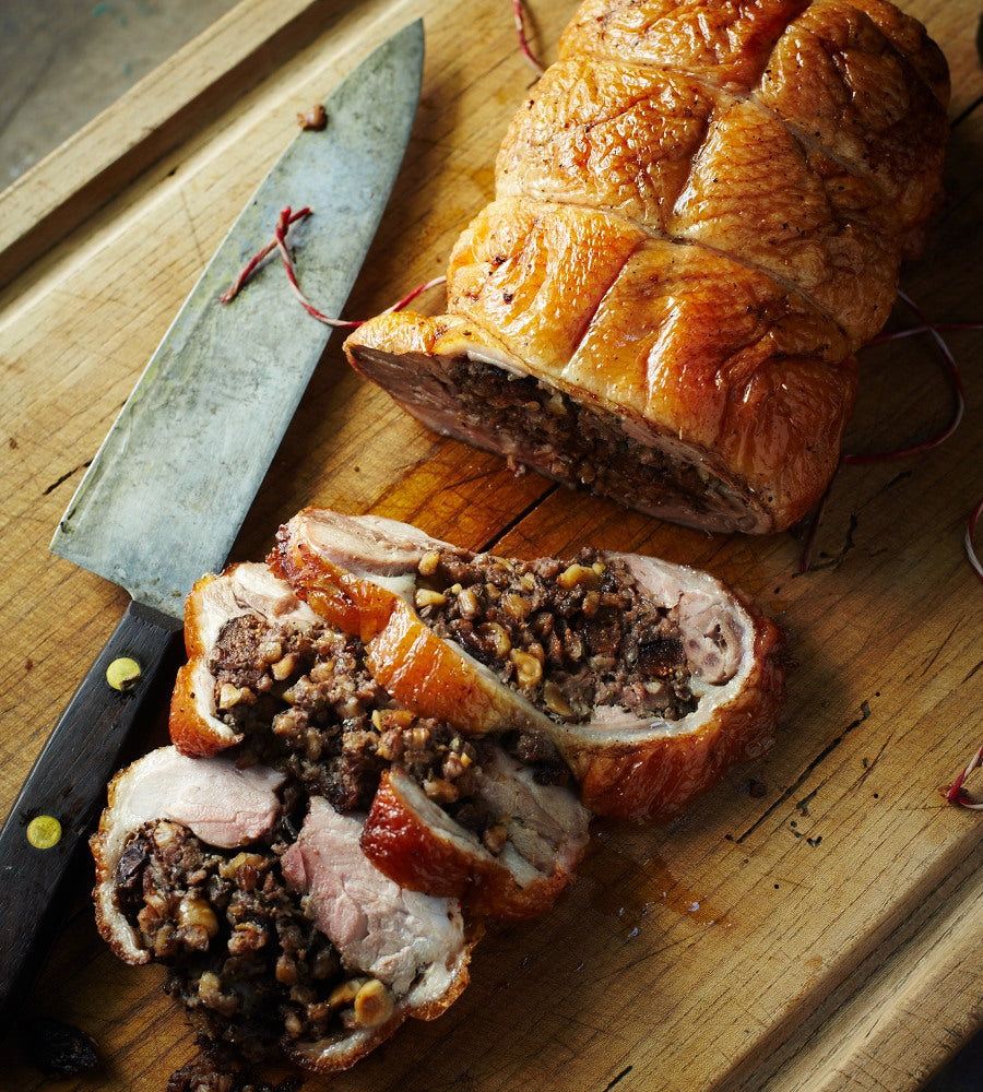 A stuffed duck roll on a wooden cutting board with three cut slices and a chef's knife.